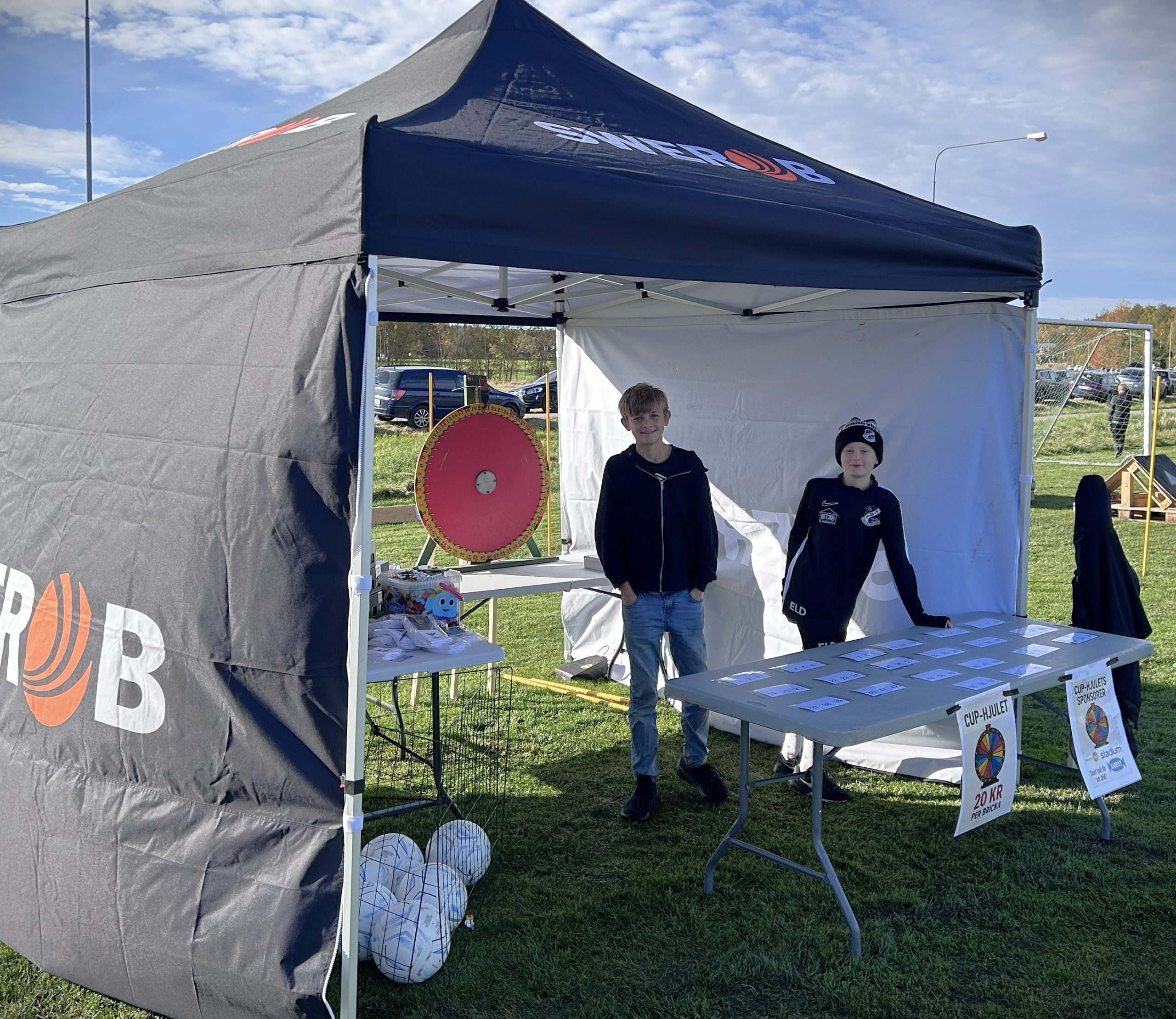 Två ungdomar står redo vid Swerobs bord med Cup-hjulet i bakgrunden